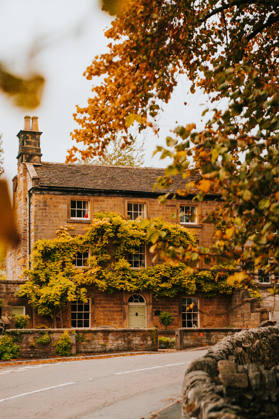 Charming stone house with brick chimney nestled amidst lush greenery and vibrant autumn foliage