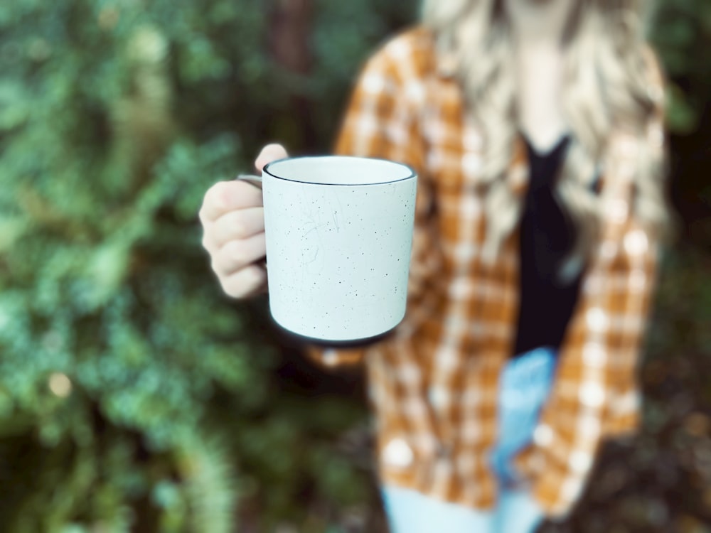 woman in black jacket holding white ceramic mug