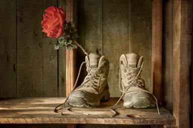 fine art photography,how to photograph a pair of hicking boots and a rose propped inside of one on the dusty shelf of a cabin.; white leather lace up boots