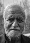 A black and white portrait of an elderly man with deep wrinkles and expressive eyes.