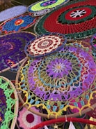 A collection of intricately woven dreamcatchers, each displaying unique patterns and vibrant colors, is arranged overlapping one another. The foreground features a prominent dreamcatcher with a purple and yellow floral-like pattern, surrounded by others in red, green, and blue, each showcasing distinct designs.