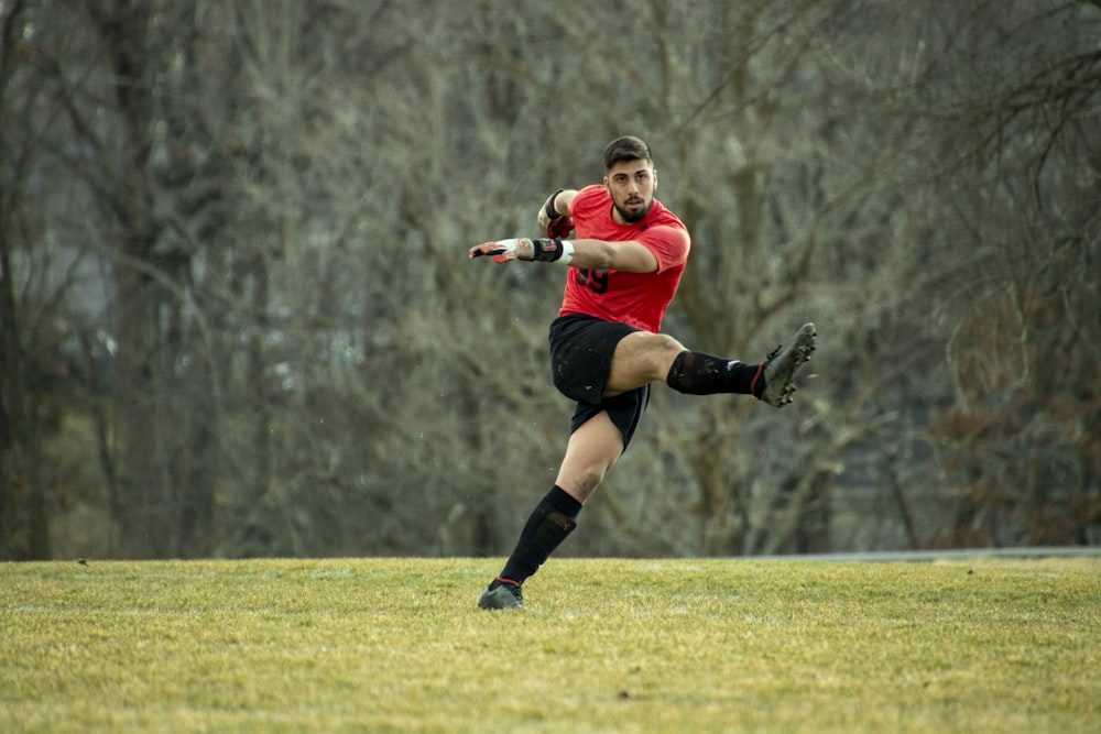 woman in red shirt and black shorts running on green grass field during daytime