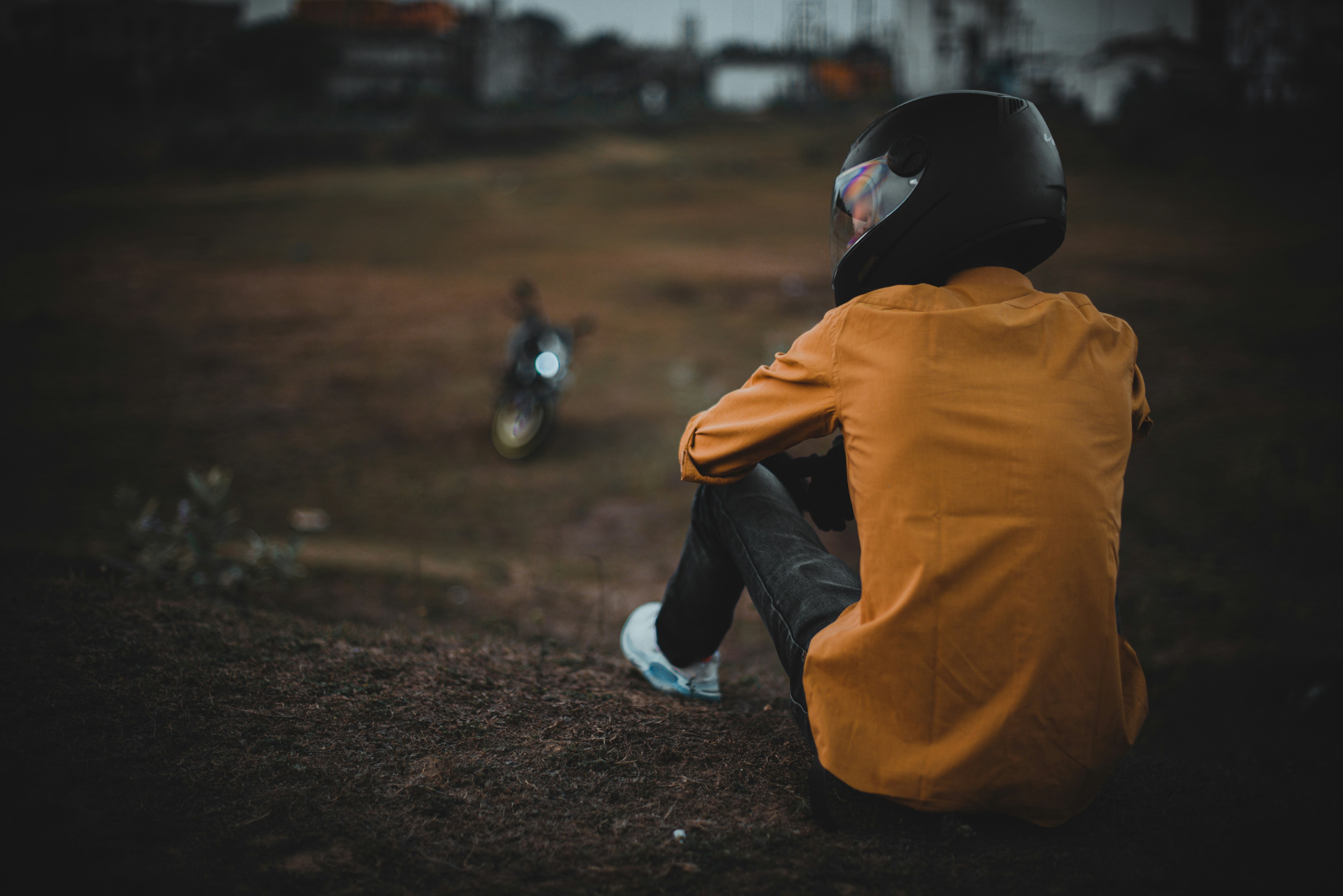 person in yellow jacket and blue denim jeans sitting on ground during daytime
