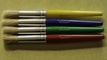 Four paintbrushes are aligned horizontally on a textured, light green surface. Each brush has a metallic ferrule and a brightly colored handle, with colors in yellow, blue, green, and red from top to bottom. The brand name 'CREATIVE PL' is printed on each handle.