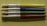 Four paintbrushes are aligned horizontally on a textured, light green surface. Each brush has a metallic ferrule and a brightly colored handle, with colors in yellow, blue, green, and red from top to bottom. The brand name 'CREATIVE PL' is printed on each handle.