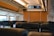Rows of empty seats inside a train cabin, featuring modern headrests and personal screens. Overhead, a digital display board provides travel information. Large windows allow natural light to fill the space, while wooden panels add a warm touch.