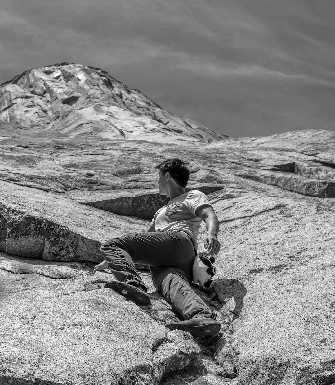 grayscale photo of woman in tank top and pants sitting on rock