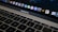 A close-up view of a MacBook Pro keyboard and screen with various application icons displayed on the dock. The keyboard has a black finish with white letters, and the screen shows icons like Safari, Mail, and Finder. The lighting is dim, providing a cozy atmosphere.