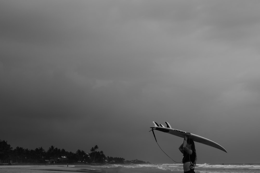 grayscale photo of man in long sleeve shirt and pants holding a surfboard