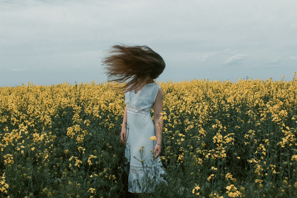 woman in white dress standing on yellow flower field during daytime