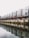 A row of modern, uniquely designed apartment buildings with a silver metallic exterior, featuring multiple small windows. The structures are built alongside a tranquil body of water reflecting them. The sky appears overcast, adding to the muted ambiance of the scene.