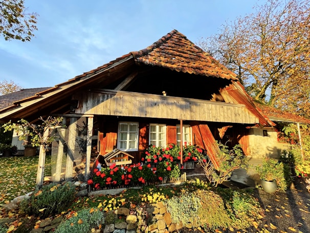 Cozy rustic cabin exterior surrounded by trees and flowers on a sunny day