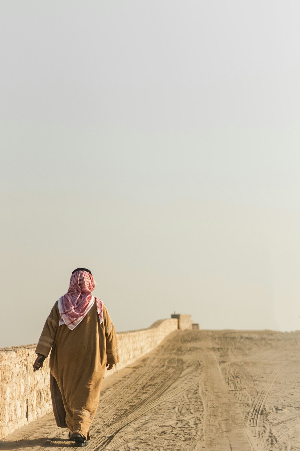 donna in hijab marrone in piedi sulla sabbia marrone durante il giorno