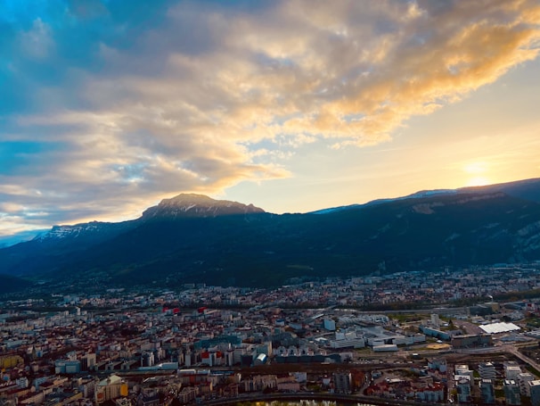 A sweeping aerial shot of the Denver skyline at sunset, with the Rocky Mountains glowing in the background.