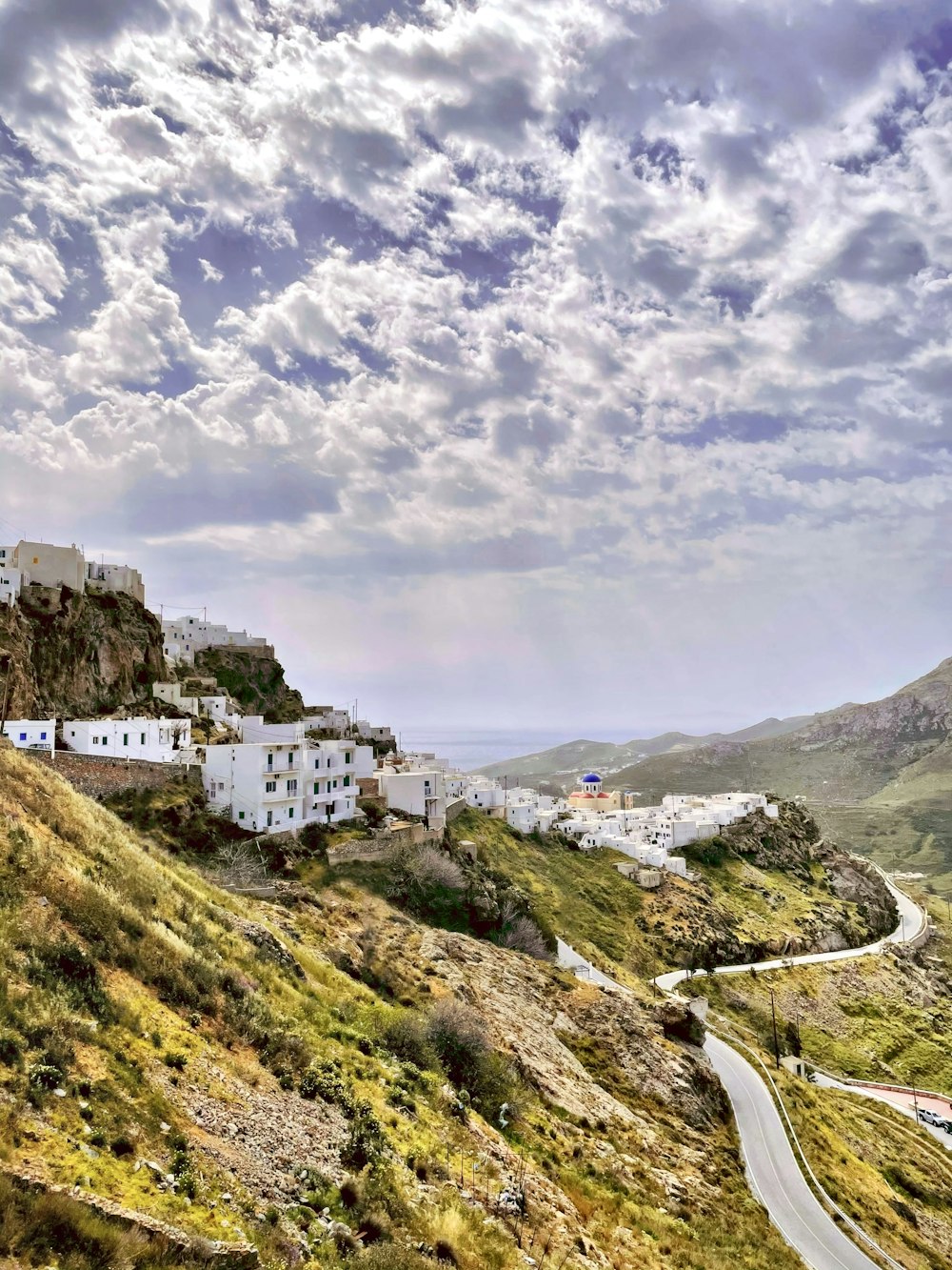 white and brown concrete buildings on green mountain under white clouds during daytime