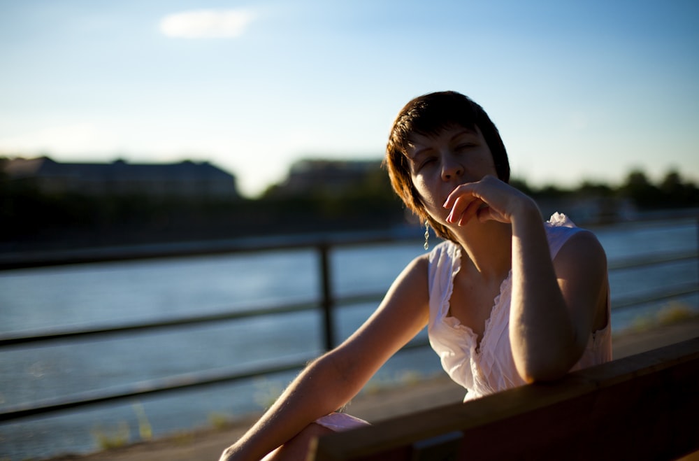 woman in white sleeveless dress sitting on brown wooden bench during daytime
