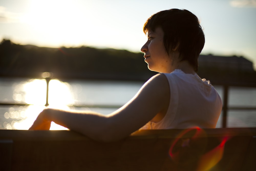woman in white tank top sitting on brown wooden chair during sunset