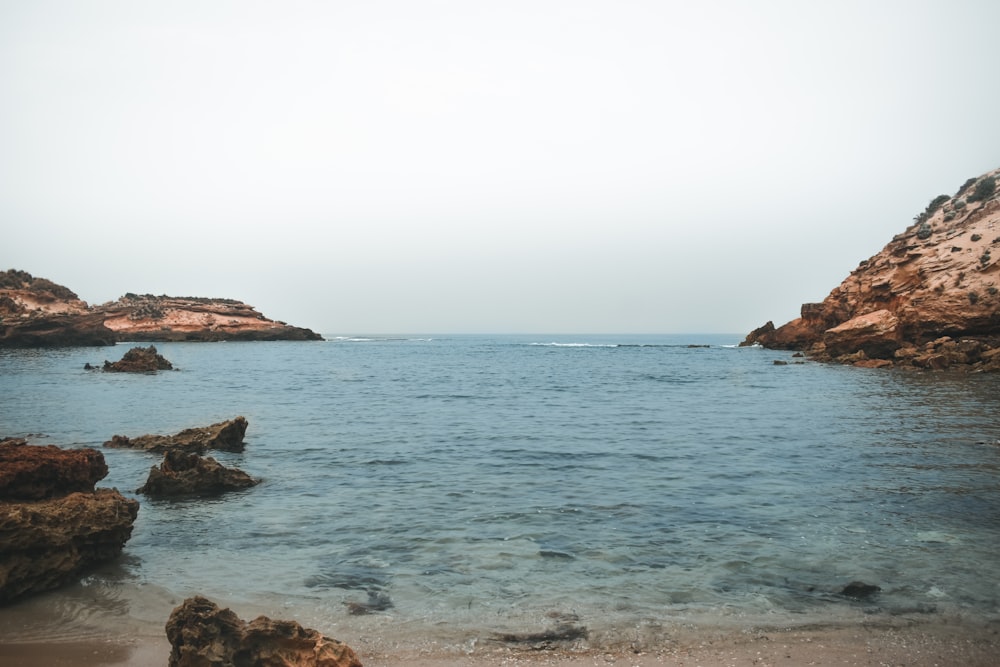 brown rock formation on sea under white sky during daytime