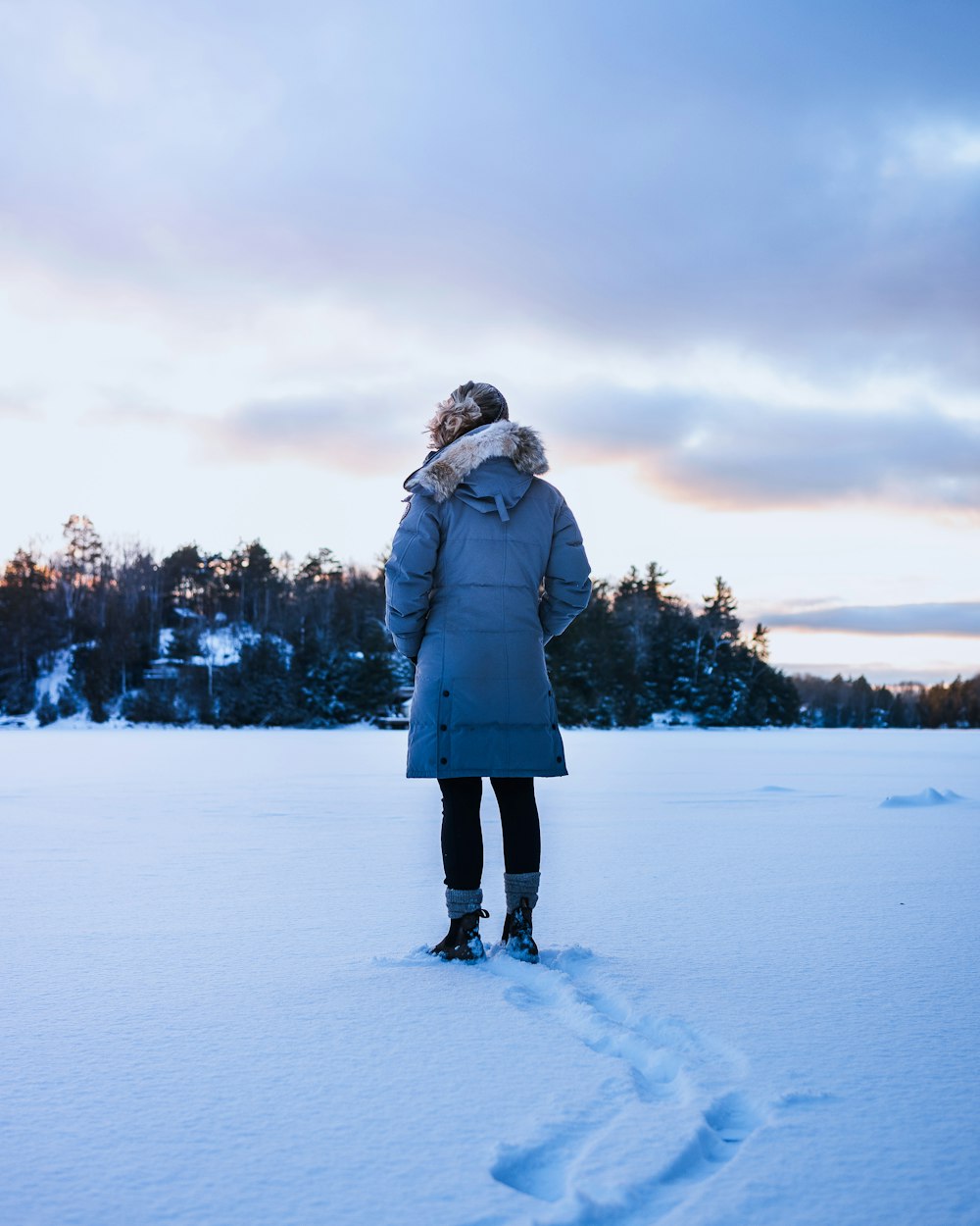 woman in gray coat standing on snow covered ground during daytime