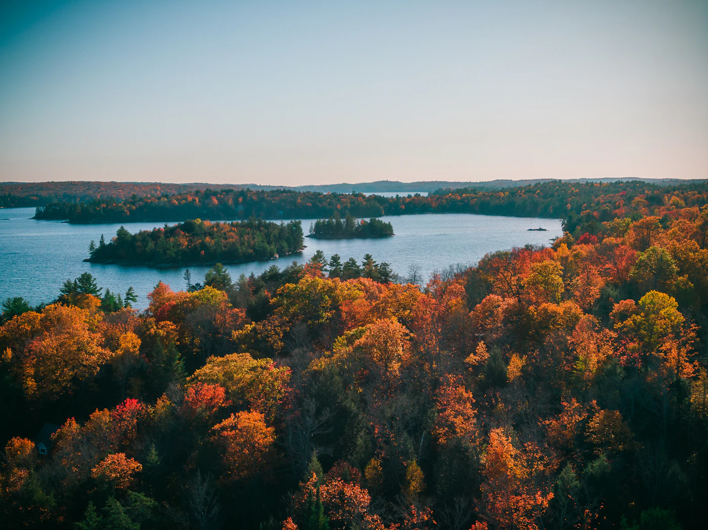 An aerial view of an Ontario lake ringed by green and gold autumn forest