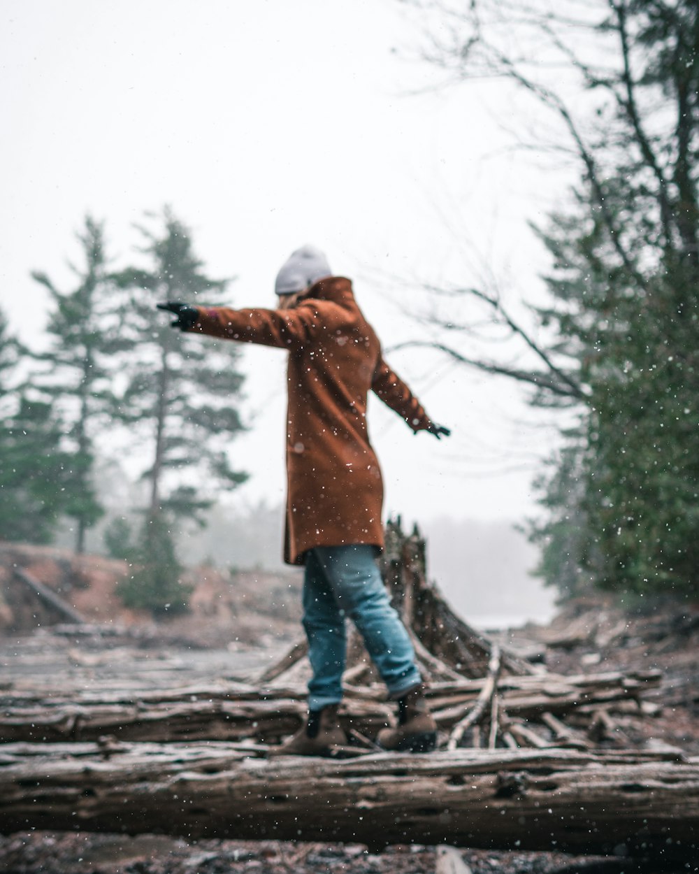 man in orange jacket and blue denim jeans standing on tree log during daytime