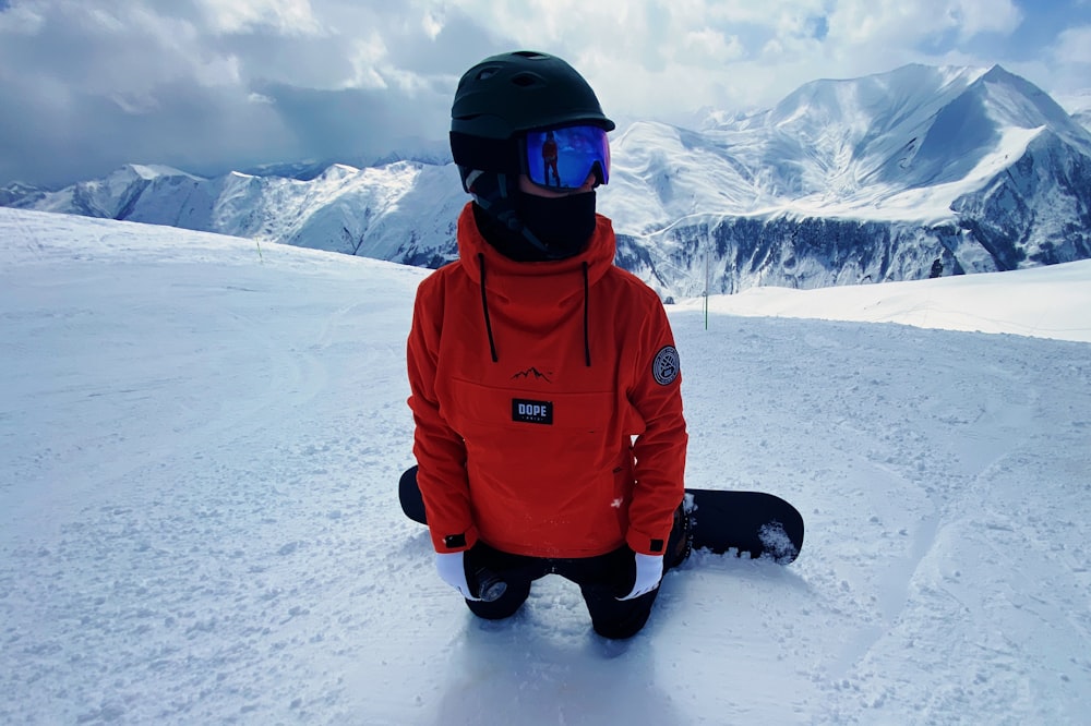 man in red jacket and black pants standing on snow covered ground during daytime