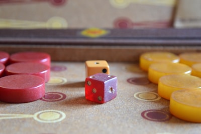 A collection of game pieces, including a red die, an orange die, and several circular red and yellow checkers, is placed on a board with circular patterns.