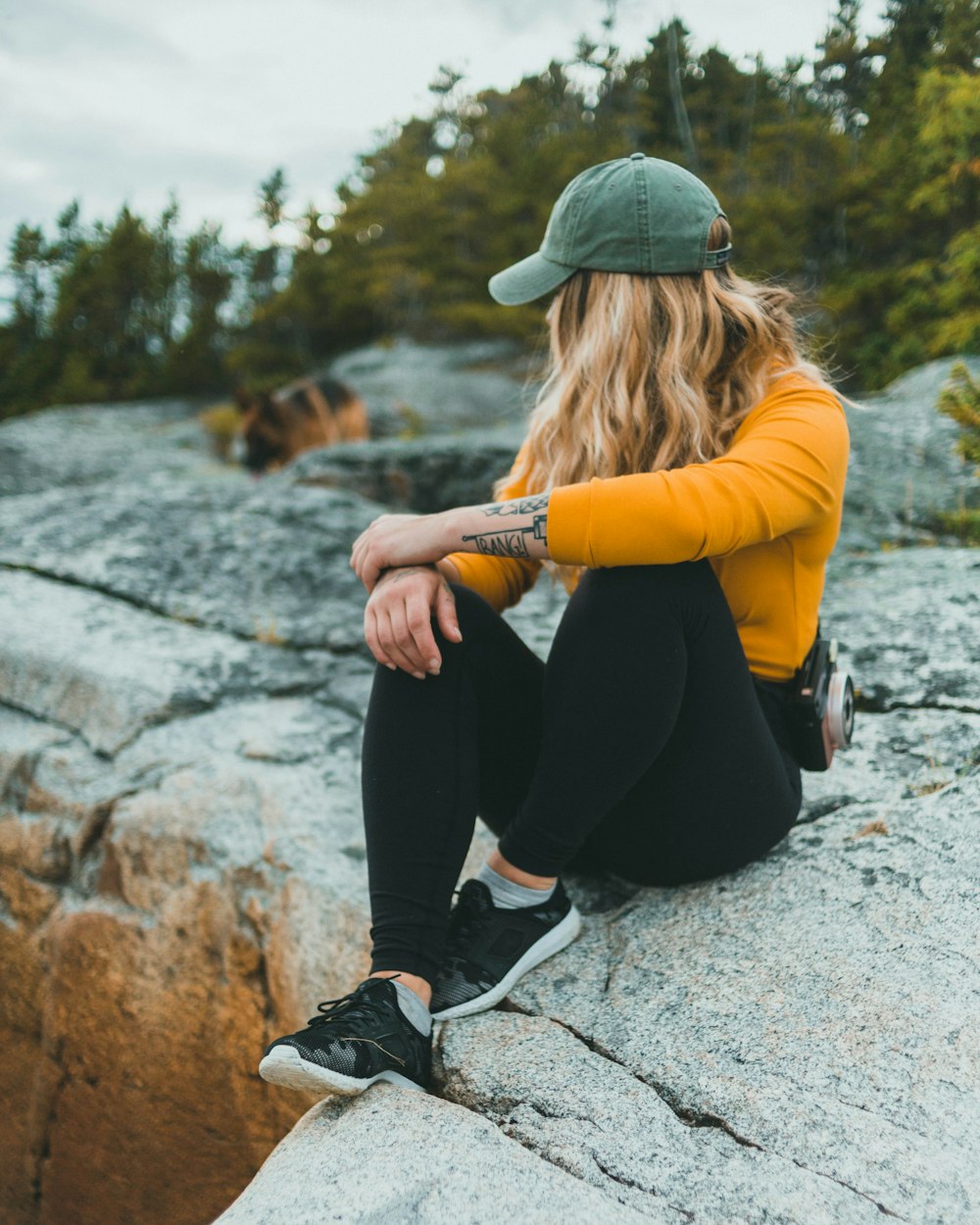 woman in yellow long sleeve shirt and black pants sitting on gray concrete pavement during daytime