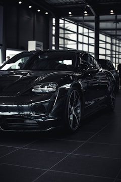 A sleek, modern car with a glossy black finish is parked inside a spacious, well-lit showroom. The car's aerodynamic design and bold features are highlighted by the indoor lighting.