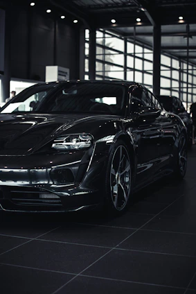 A sleek black luxury car parked in a modern showroom with soft golden lighting highlighting its curves.