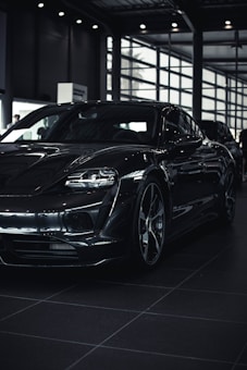A sleek, modern car with a glossy black finish is parked inside a spacious, well-lit showroom. The car's aerodynamic design and bold features are highlighted by the indoor lighting.