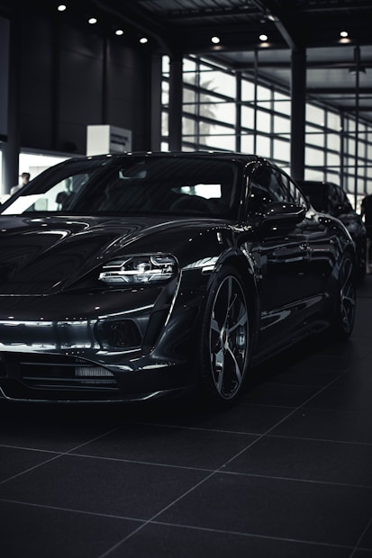 A sleek, modern car with a glossy black finish is parked inside a spacious, well-lit showroom. The car's aerodynamic design and bold features are highlighted by the indoor lighting.