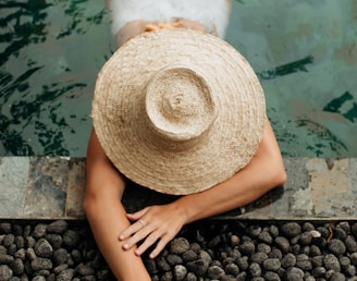 person wearing brown straw hat sitting on black stones near body of water during daytime