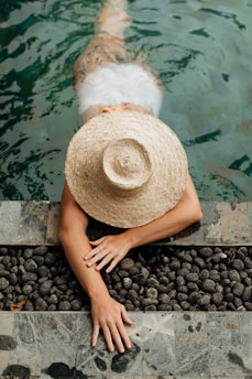 person wearing brown straw hat sitting on black stones near body of water during daytime