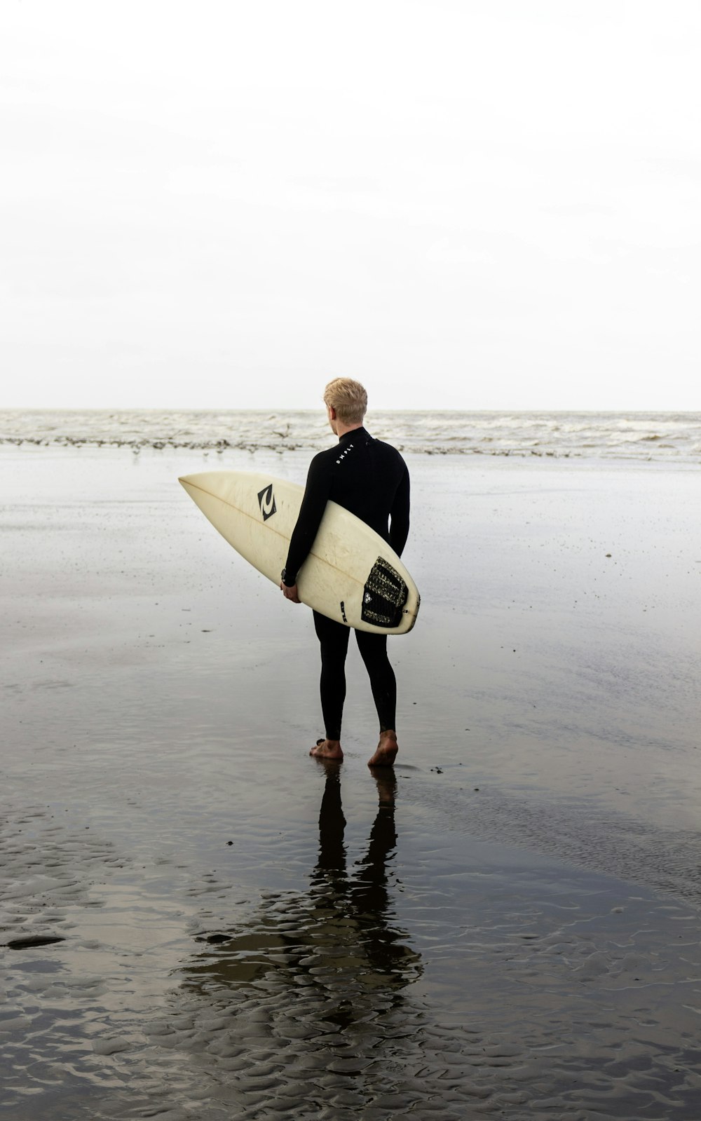 man in black jacket holding white surfboard walking on beach during daytime