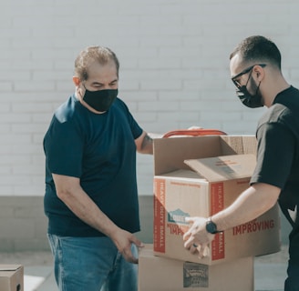 man in blue crew neck t-shirt standing beside brown cardboard boxes