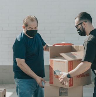 man in blue crew neck t-shirt standing beside brown cardboard boxes