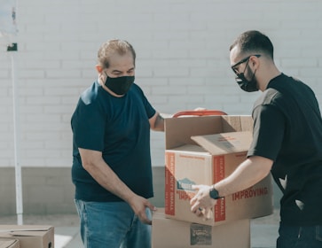 man in blue crew neck t-shirt standing beside brown cardboard boxes