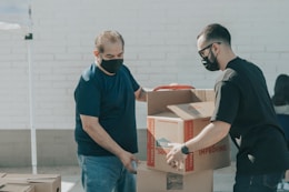man in blue crew neck t-shirt standing beside brown cardboard boxes