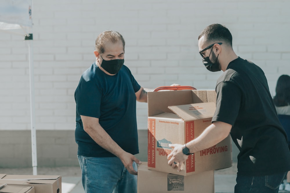 man in blue crew neck t-shirt standing beside brown cardboard boxes