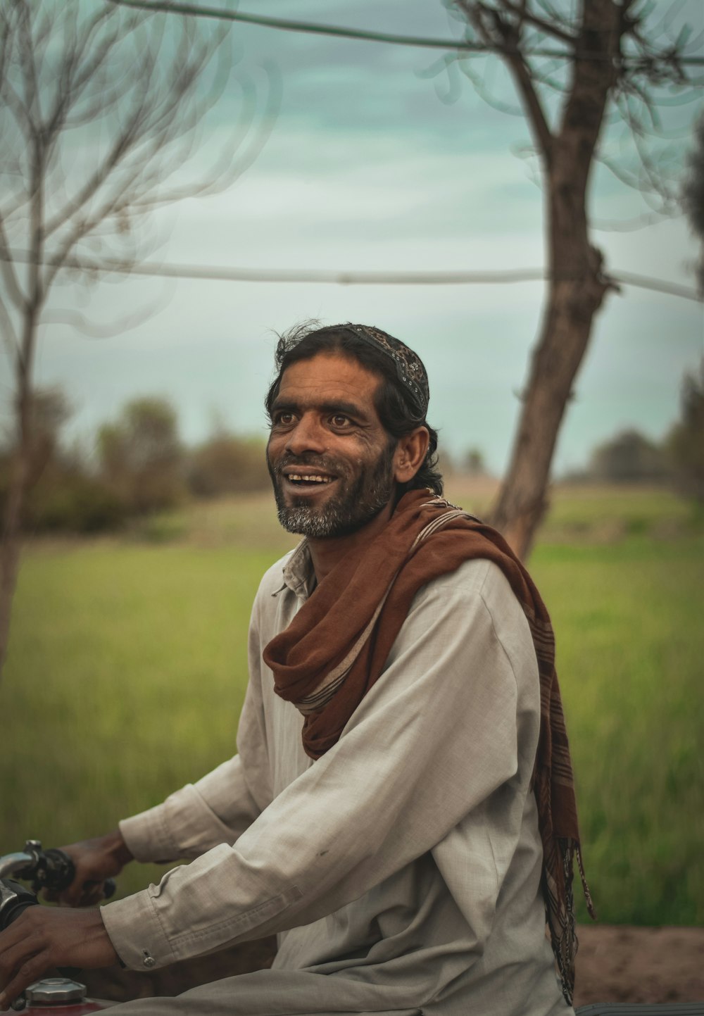 man in white long sleeve shirt and brown scarf standing near bare tree during daytime