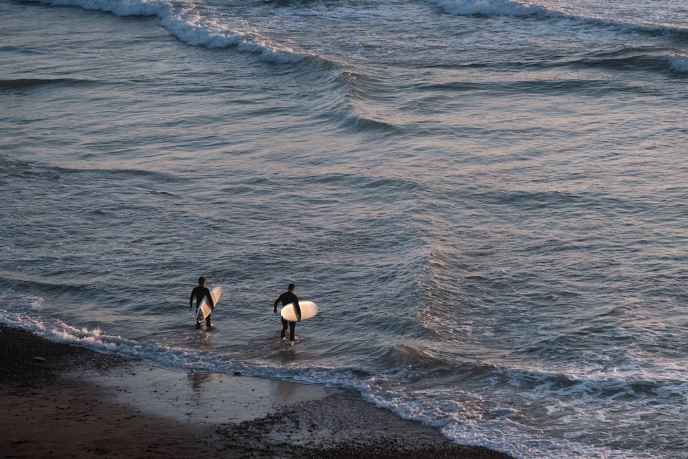 2 person in black wet suit standing on sea shore during daytime