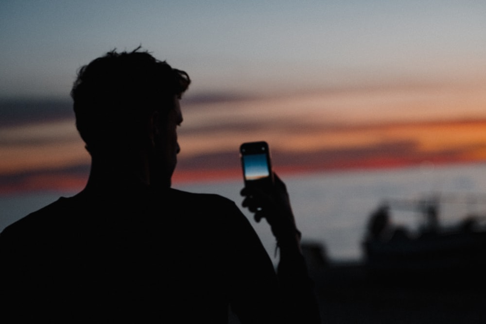 a man holding a cell phone in front of a sunset