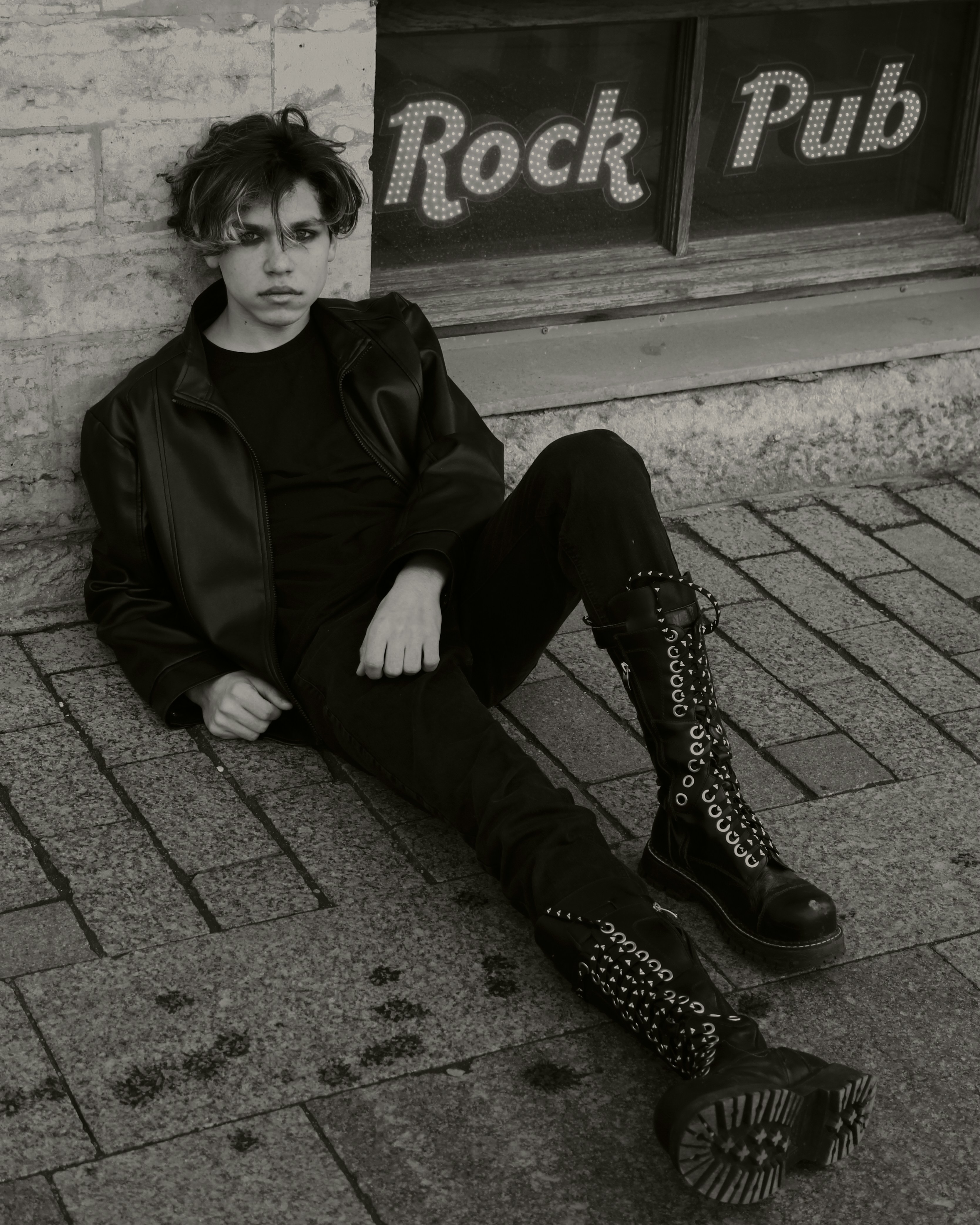woman in black coat and black pants sitting on concrete pavement