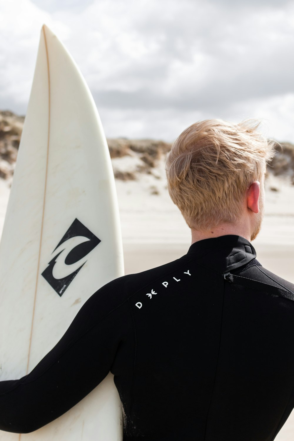 man in black jacket holding white surfboard