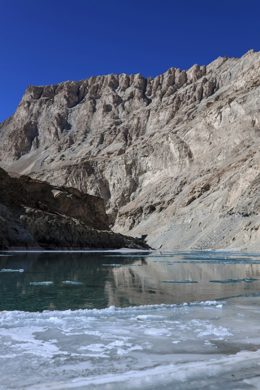 brown rocky mountain beside body of water during daytime