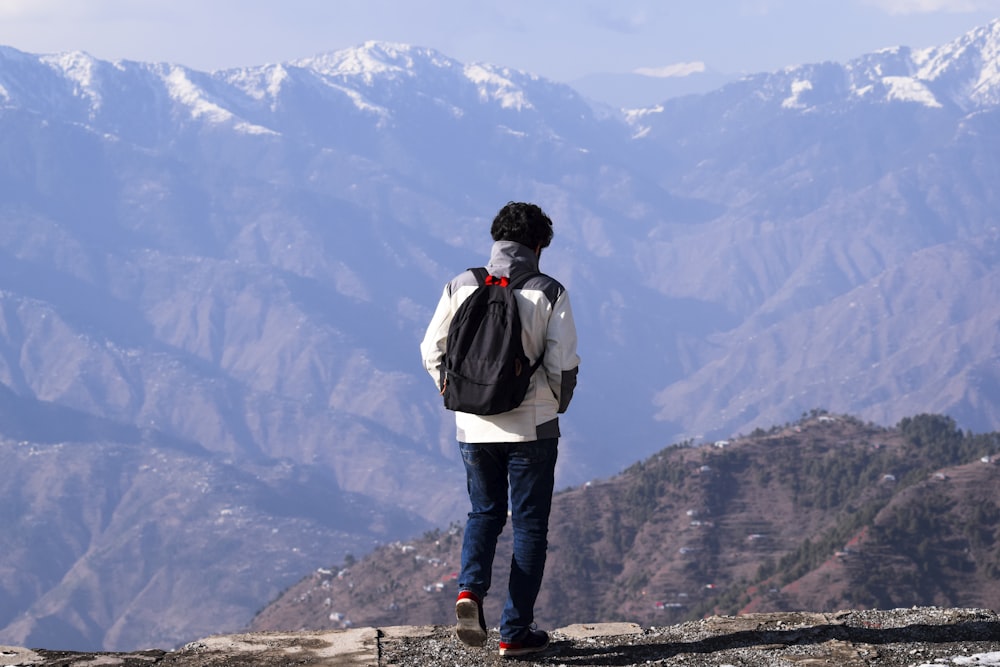 man in white jacket and blue denim jeans standing on rock formation during daytime