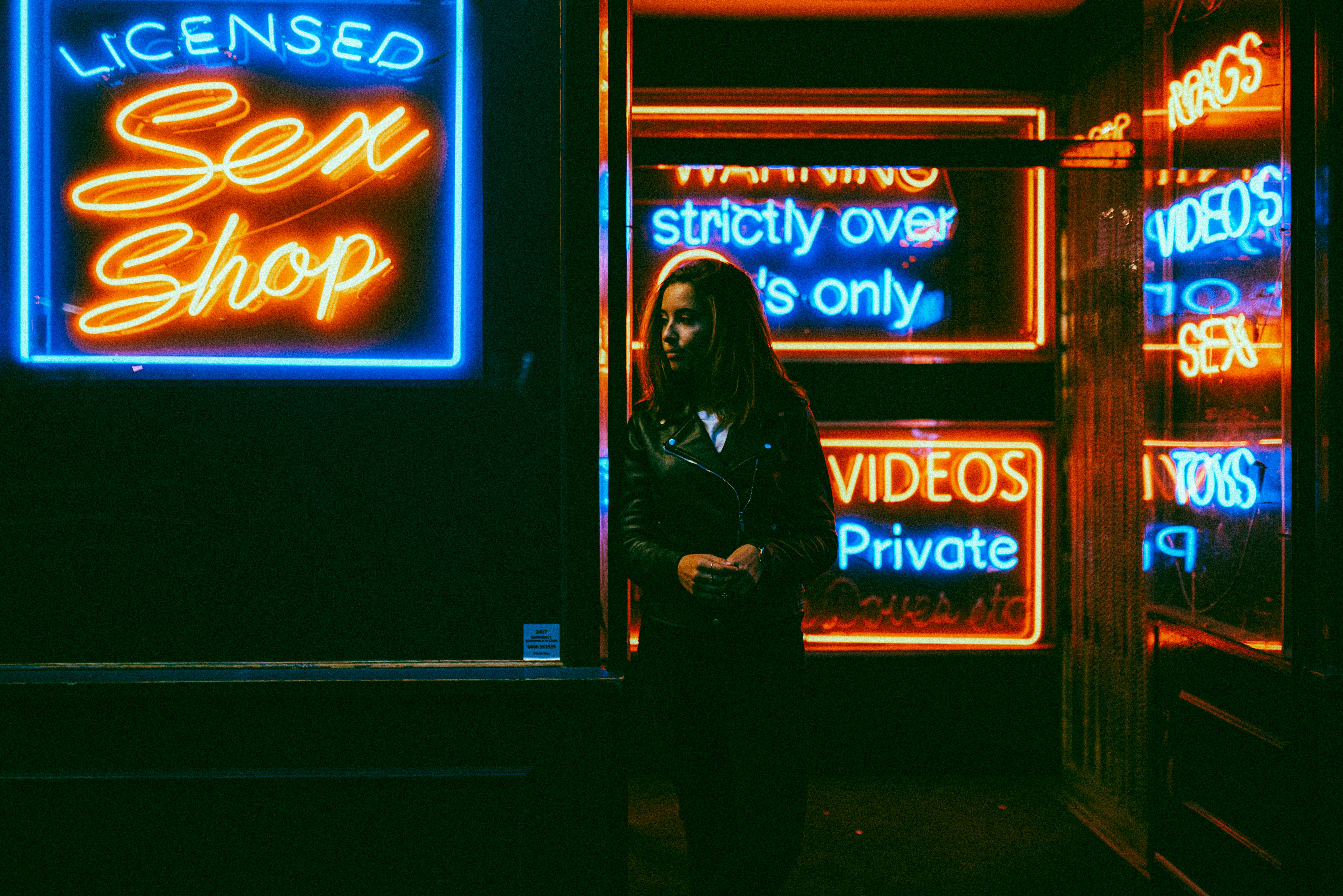 woman in black jacket standing in front of blue and red UNKs neon signage