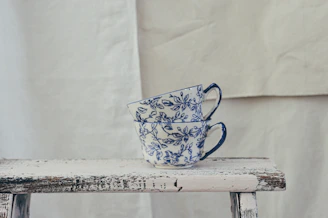 A pair of hand-thrown cups in vibrant blues and greens, stacked casually beside a cozy knitted blanket.