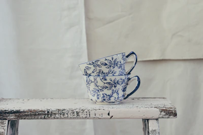 A pair of hand-thrown cups in vibrant blues and greens, stacked casually beside a cozy knitted blanket.